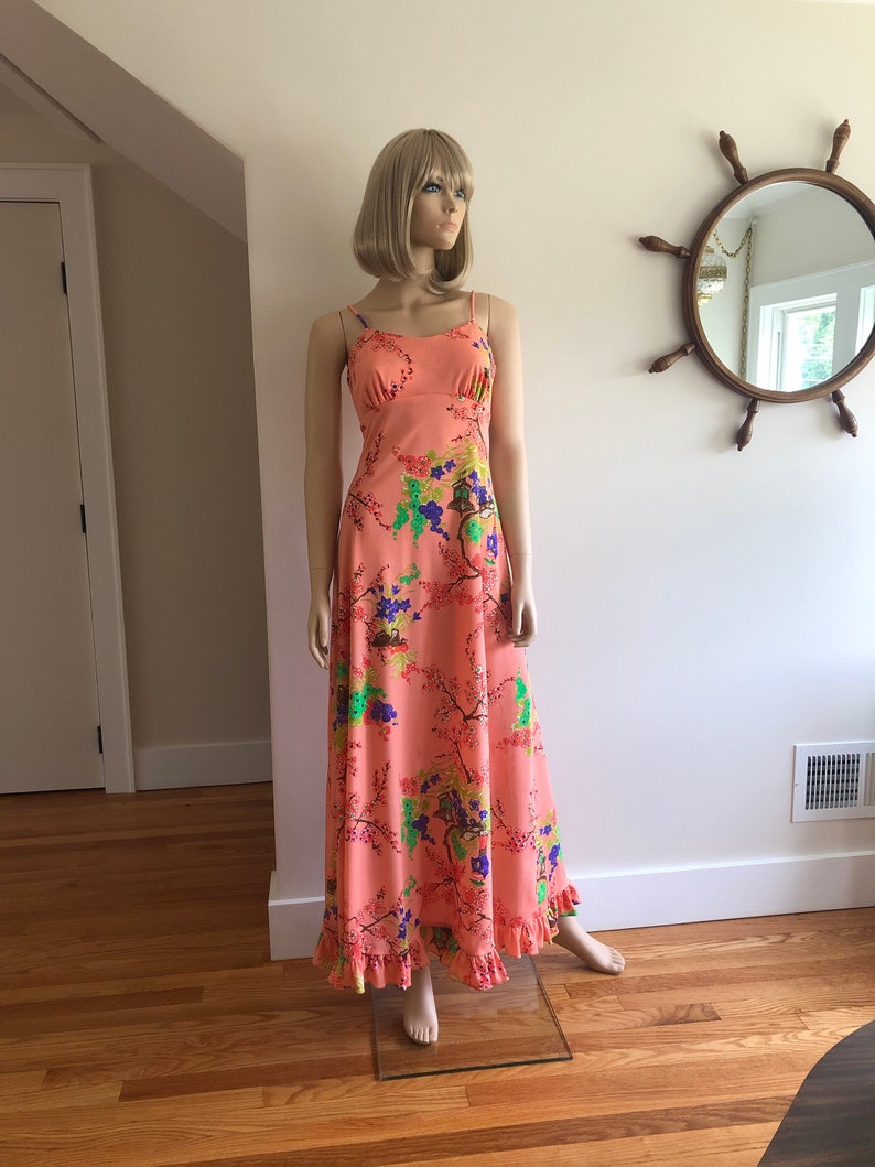 May include: A long, peach-colored maxi dress with a floral print. The dress has thin straps and a ruffled hem.
