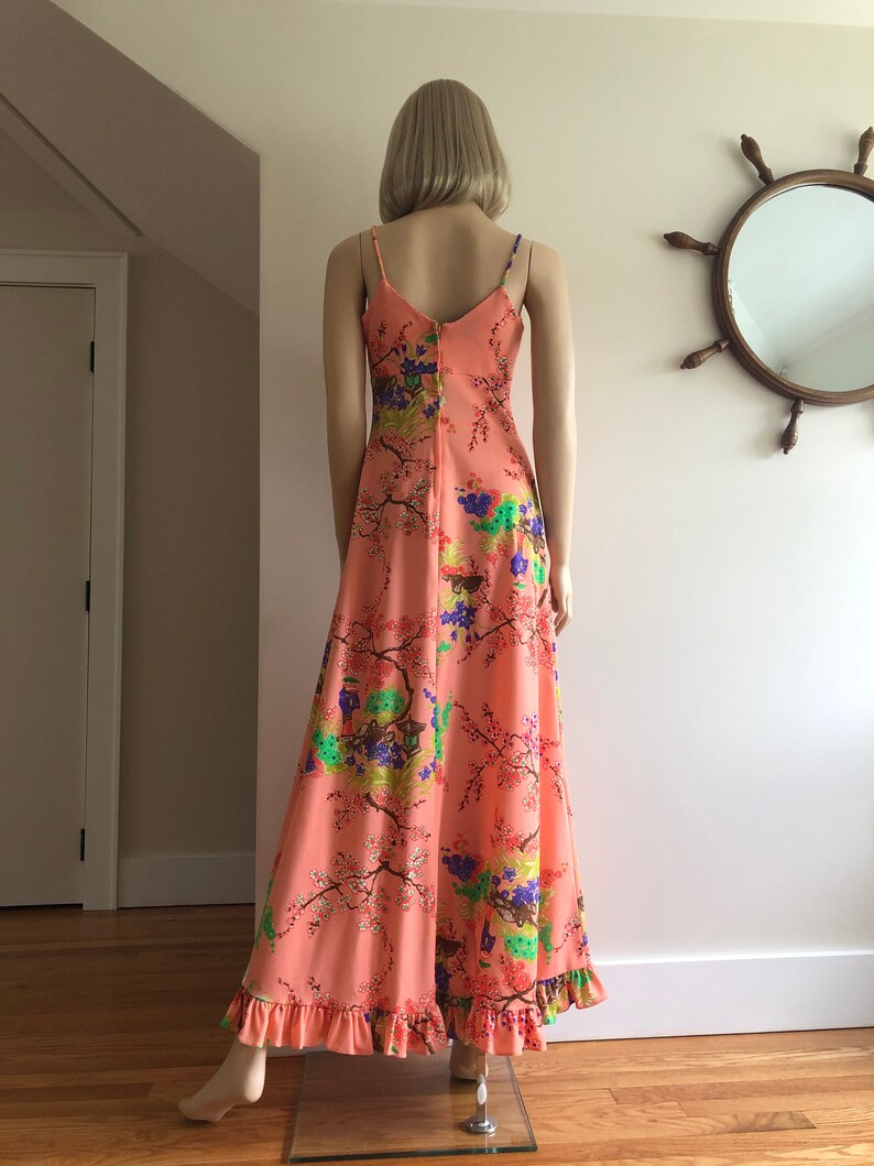 May include: A long, peach-colored maxi dress with a floral print featuring pink, green, blue, and purple flowers. The dress has thin straps and a ruffled hem.