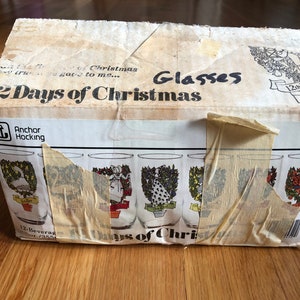 May include: A box of 12 Anchor Hocking "12 Days of Christmas" glasses. The box is white with red and black text. The glasses are clear with a festive design.