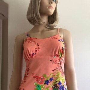 May include: A sleeveless, peach-colored dress with a floral print featuring cherry blossoms, green leaves, and purple flowers. The dress has a fitted bodice and a flowing skirt.