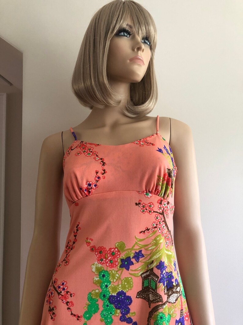 May include: A sleeveless, peach-colored dress with a floral print featuring cherry blossoms, green leaves, and purple flowers. The dress has a fitted bodice and a flowing skirt.