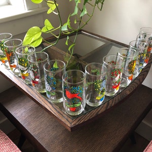 May include: Set of 12 vintage glass tumblers with colorful Christmas tree designs. Each glass features a different bird and a festive banner.