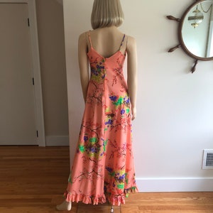 May include: A long, peach-colored maxi dress with a floral print. The dress has thin straps and a ruffled hem.