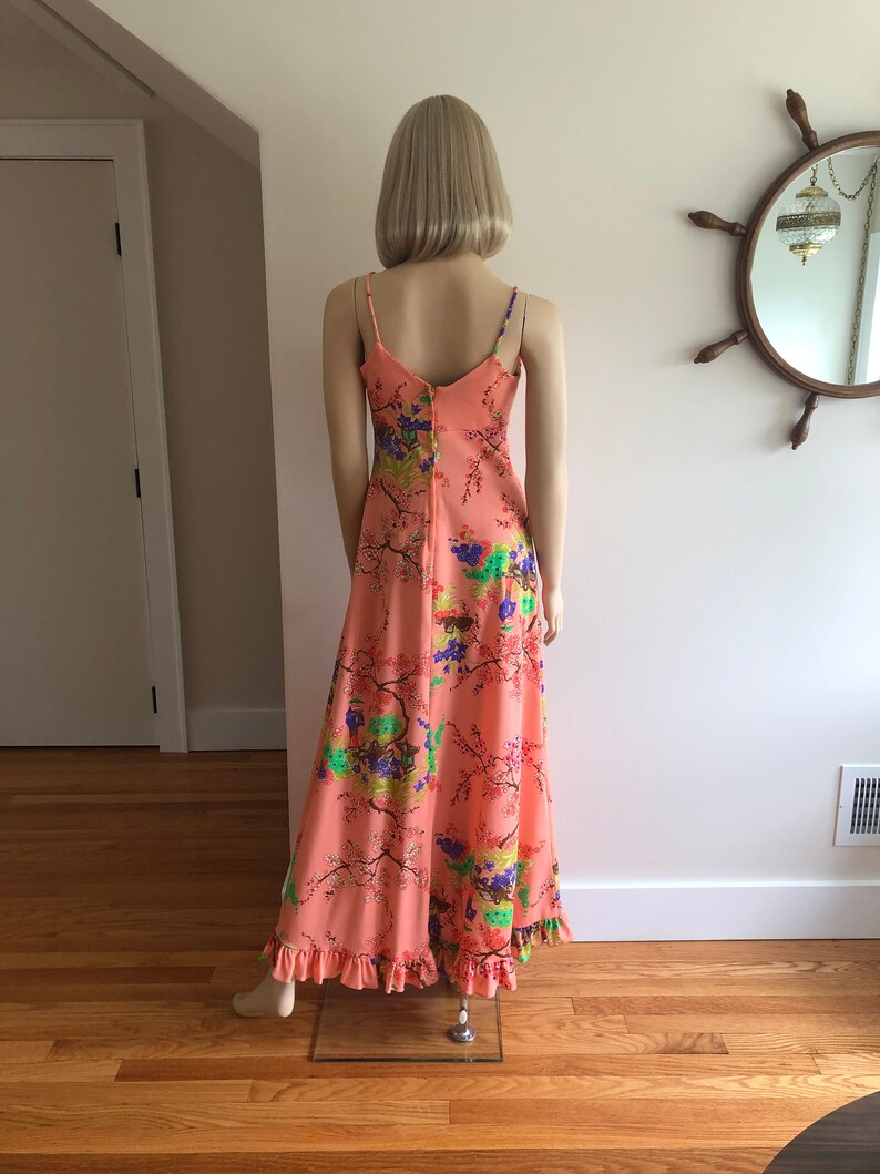 May include: A long, peach-colored maxi dress with a floral print. The dress has thin straps and a ruffled hem.