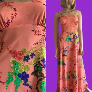 May include: A long, peach-colored maxi dress with a floral print featuring cherry blossoms, lanterns, and green leaves. The dress has thin straps and a ruffled hem.