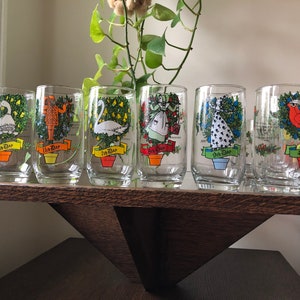 May include: Set of six clear glass tumblers with colorful illustrations of the 12 Days of Christmas. Each tumbler features a different day, with a festive design and the text "1st Day", "2nd Day", etc.