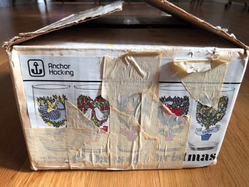 May include: A box of Anchor Hocking Christmas glasses with a white background and a red, green, and blue design. The box is labeled "Anchor Hocking" and "12 Days of Christmas".