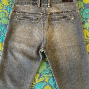 May include: Faded blue denim jeans with a classic five-pocket design. The jeans feature a button and zipper closure, belt loops, and two back pockets. The back of the jeans is visible, showing the stitching and the brand label.