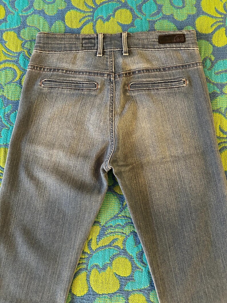 May include: Faded blue denim jeans with a classic five-pocket design. The jeans feature a button and zipper closure, belt loops, and two back pockets. The back of the jeans is visible, showing the stitching and the brand label.