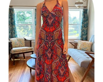 May include: A halter-neck maxi dress with a vibrant paisley pattern in red, blue, and gold. The dress features a V-neckline and a flowing skirt. The dress is displayed on a mannequin.