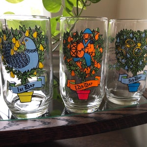 May include: Set of six clear glass tumblers with colorful illustrations of the 12 Days of Christmas. Each tumbler features a different day, with a corresponding number and the text "Day".