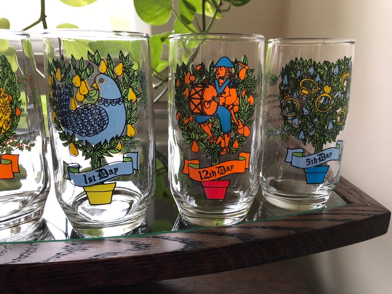May include: Set of six clear glass tumblers with colorful illustrations of the 12 Days of Christmas. Each tumbler features a different day, with a corresponding number and the text "Day".