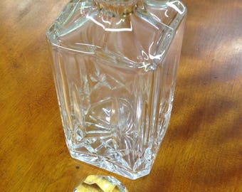 May include: A clear glass decanter with a faceted design and a gold-colored stopper. The stopper is a round ball with a faceted design.
