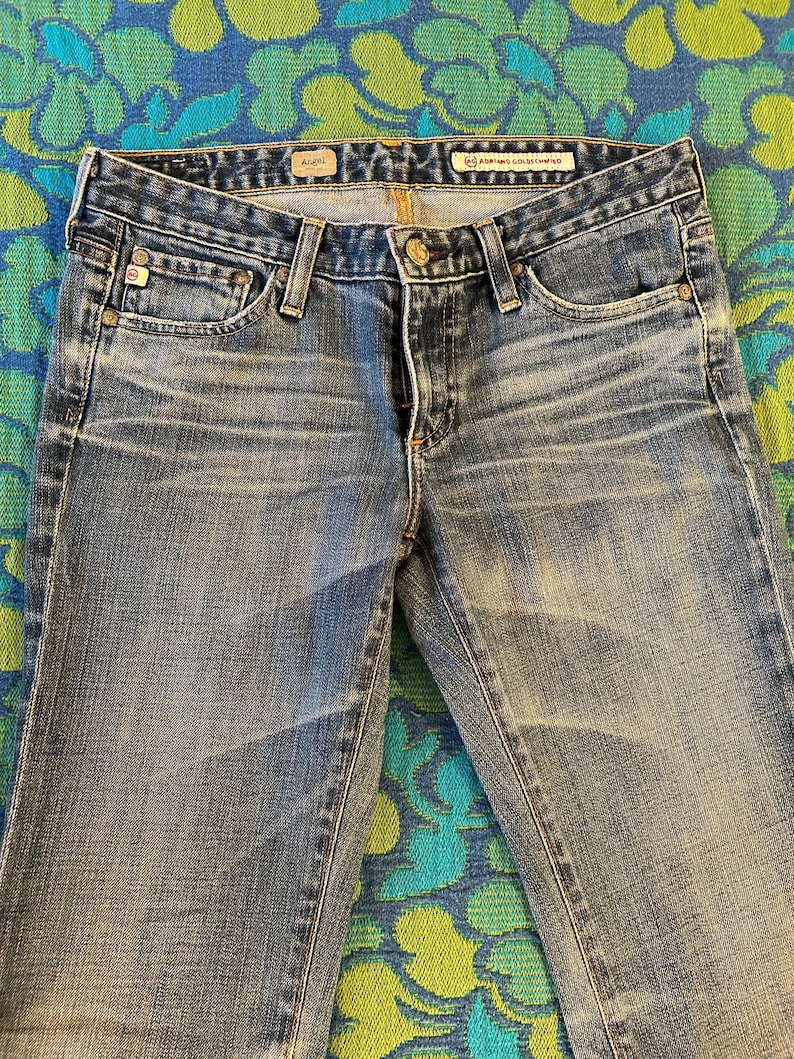 May include: Close-up of light blue denim jeans. The jeans have a classic five-pocket design, a button and zip closure, and belt loops. The jeans are slightly faded, with subtle wear marks.