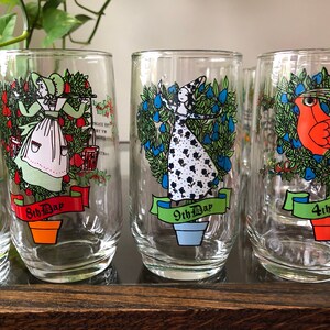 May include: Set of six clear glass tumblers with colorful illustrations of the 12 Days of Christmas. Each glass features a different day, with a festive design and the text "Day" and the corresponding number.