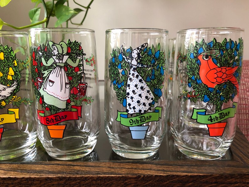May include: Set of six clear glass tumblers with colorful illustrations of the 12 Days of Christmas. Each glass features a different day, with a festive design and the text "Day" and the corresponding number.
