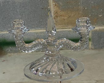 May include: A clear glass candle holder with two arms and a central spire. The holder has a textured, rope-like design and a scalloped base.