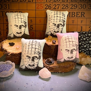 May include: Four decorative pillows with a black and white image of a character with a grid pattern on their head. The pillows are on a wooden surface with a calendar in the background. The calendar shows the months of October and November.