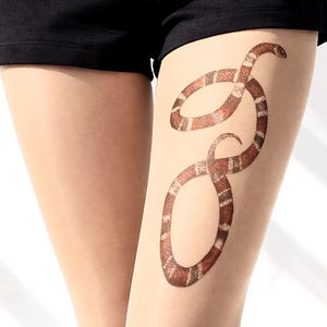 May include: Nude-coloured sheer tights featuring a brown and white snake design printed on the thigh. The snake design has scale details and curves. The tights are worn with black shorts.