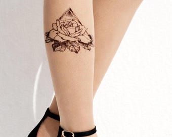 May include: A black and white temporary tattoo of a rose within a triangle is displayed on a leg. The leg is wearing black high-heeled sandals with an ankle strap. The background is a plain white wall.