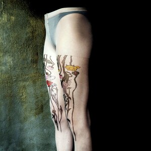 May include: A pair of sheer tights with a floral design printed on the legs. The design features stylized flowers in shades of pink, yellow, and brown.