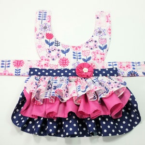 May include: A dog dress with a floral pattern in pink, white, and blue. The dress has a layered skirt with a navy blue polka dot design and a pink ruffle. A pink flower is attached at the waist.