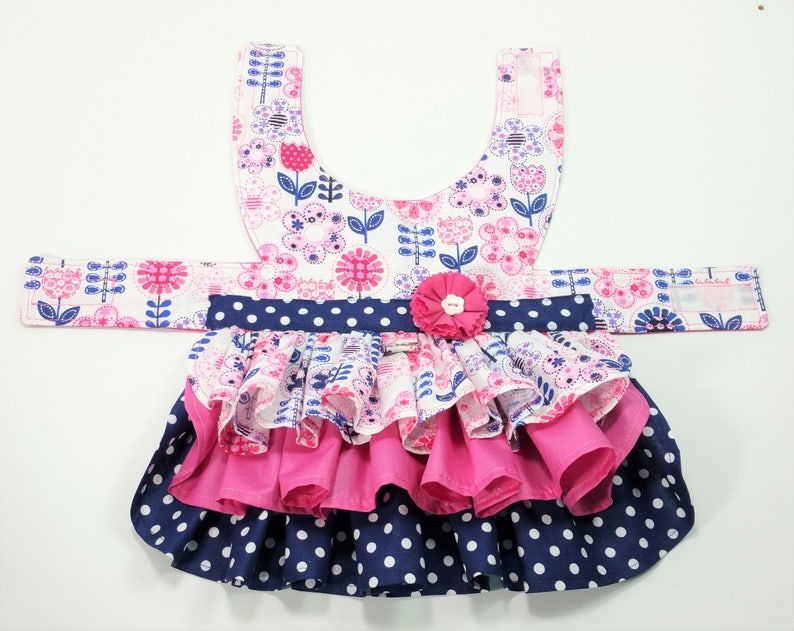 May include: A dog dress with a floral pattern in pink, white, and blue. The dress has a layered skirt with a navy blue polka dot design and a pink ruffle. A pink flower is attached at the waist.