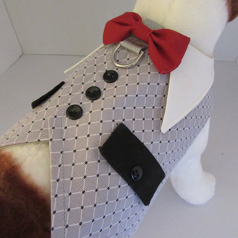 Puede incluir: Un chaleco gris para perro con cuello blanco y pajarita roja. El chaleco tiene un patr&oacute;n de cuadros blanco y negro y botones negros.
