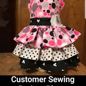 May include: A tiered dog dress featuring a pink, black, and white polka dot design. It has a black belt with a Mickey Mouse emblem and a white flower. The text "Customer Sewing Project Photo" is displayed at the bottom.
