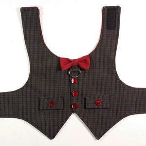 Puede incluir: Un chaleco para perro de cuadros negros y grises con una pajarita roja y un anillo plateado. El chaleco tiene dos bolsillos y cierres de velcro.