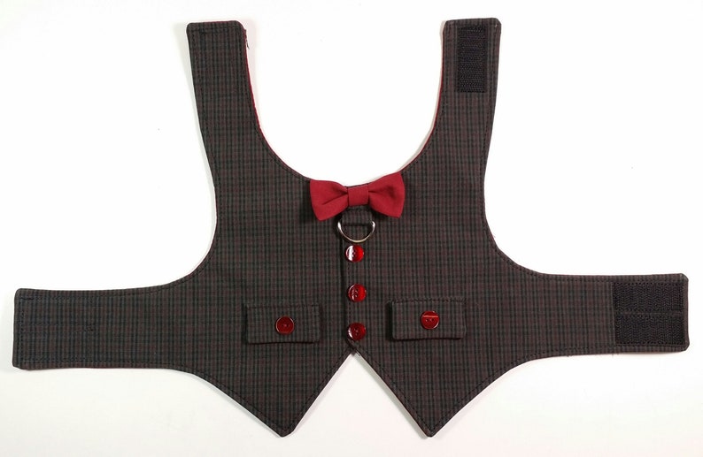 Puede incluir: Un chaleco para perro de cuadros negros y grises con una pajarita roja y un anillo plateado. El chaleco tiene dos bolsillos y cierres de velcro.