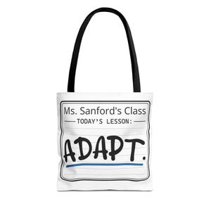 May include: A white tote bag with black handles featuring a graphic design that mimics a lined notebook page. The text reads Ms. Sanford's Class, TODAY'S LESSON:, and ADAPT. in large black letters, with a blue horizontal line underneath the word.
