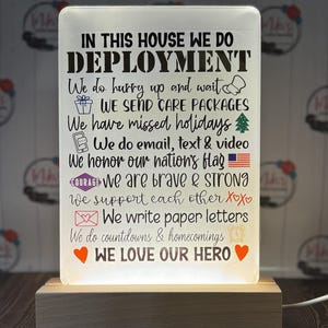 May include: A white light-up sign with the text "In this house we do deployment" and a list of phrases about supporting a loved one in the military. The sign is on a wooden base.