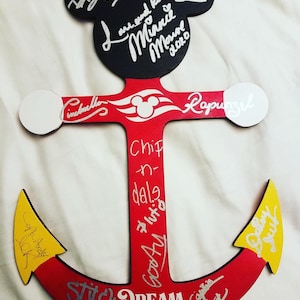 May include: A red wooden anchor with a Mickey Mouse head at the top. The anchor is decorated with silver glitter and has the words "Stitch Dream 2019" written on it. The anchor is signed by various Disney characters, including Mickey Mouse, Minnie Mouse, Cinderella, Rapunzel, Chip, Dale, Pluto, Goofy, and others.
