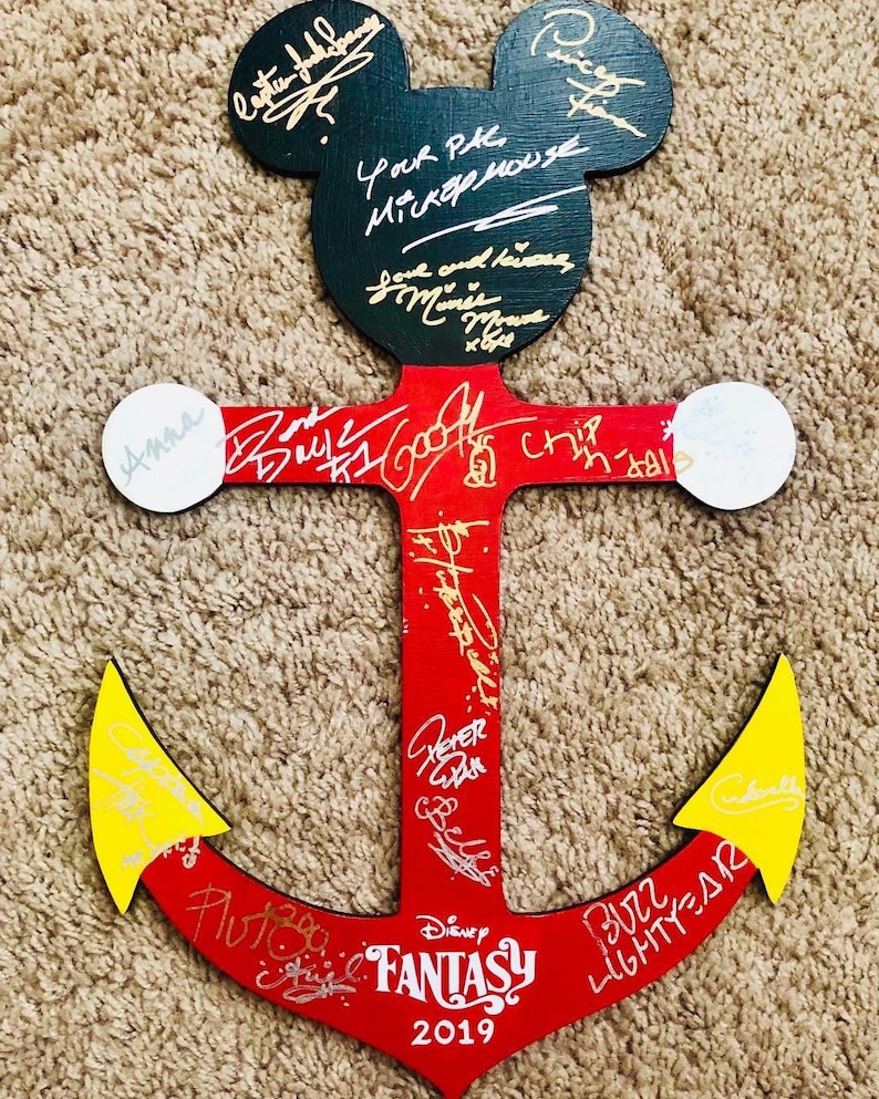 May include: A red wooden anchor with yellow tips, decorated with signatures from Disney characters. The anchor is shaped like Mickey Mouse's head with black ears. The text "Disney FANTASY 2019" is written on the anchor.