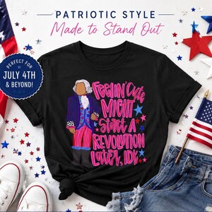 May include: A black short-sleeved t-shirt featuring a graphic of a historical figure in a blue coat and red striped pants. The text reads: Feelin' cute MIGHT START A REVOLUTION LATER, IDK. The design includes pink lettering and small blue and pink stars.