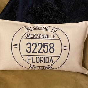 May include: A white cushion with a black circle design that says "Welcome to Jacksonville 32258 Florida My Home".