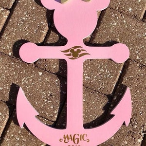 May include: Pink wooden anchor with a gold Mickey Mouse head and bow on top. The anchor has a gold Disney Cruise Line logo and the text "MAGIC 2019" on the bottom.