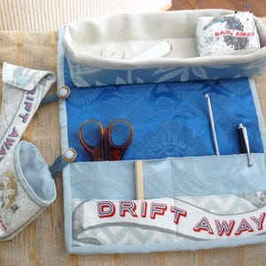 May include: A fabric sewing organiser set featuring a rectangular tray, a roll-up tool mat with pockets, and two small pouches. The items are decorated with blue and white nautical patterns and text including "SAIL AWAY" and "DRIFT AWAY".