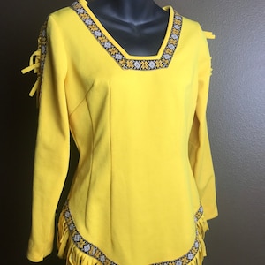 May include: A yellow long-sleeved dress with fringe trim and geometric embroidery around the neckline and hem.