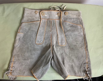May include: Gray suede shorts with decorative stitching and lace-up details on the sides. The shorts have pockets and a button closure at the waist. The shorts are a traditional style.