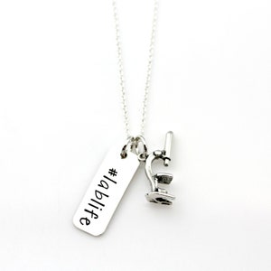 May include: A silver-colored necklace with two charms. One charm is a small microscope, and the other is a rectangular tag with the words "#lablife" in black script. The necklace hangs against a white background.