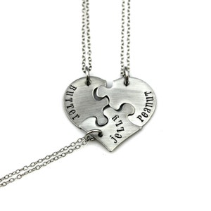 May include: Three silver puzzle pieces shaped like a heart with the names "Butter", "Jelly", and "Peanut" engraved on them. The pieces are connected by silver chains.