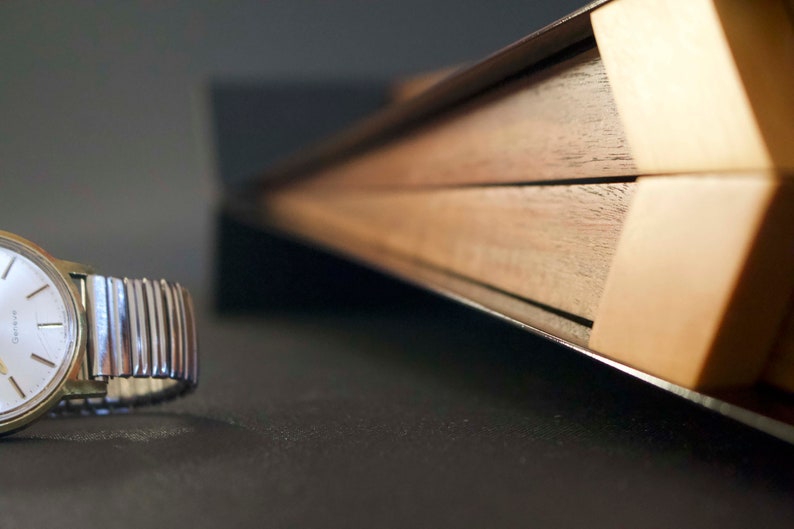 May include: A silver wristwatch with a white face and black hands. The watch is lying on a dark surface next to a wooden box with a black metal trim.