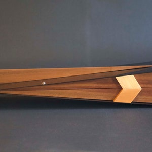 May include: A wooden box with a black metal frame and a geometric design. The box has a light wood inlay and is angled on a gray surface.
