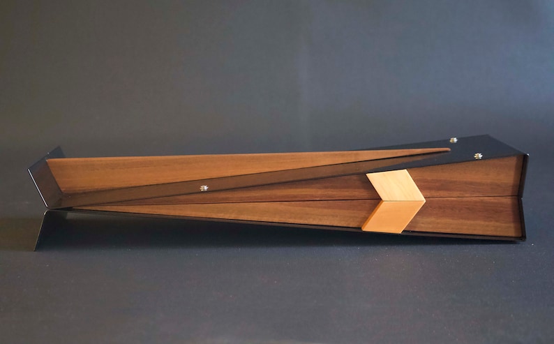 May include: A wooden box with a black metal frame and a geometric design. The box has a light wood inlay and is angled on a gray surface.