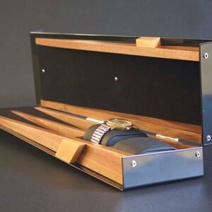 May include: A black watch box with a wooden interior and a watch resting on a cushion. The box has a hinged lid and a black exterior.