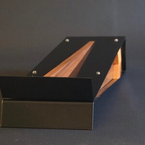 May include: A black metal stand with a wooden insert. The stand is angled and has a flat surface.