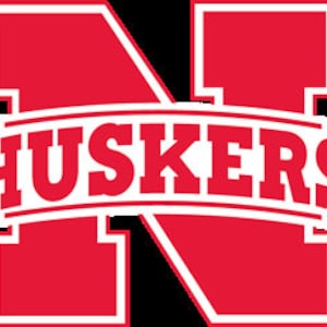 以下が含まれることがあります： 白の輪郭で「HUSKERS」という単語が書かれた赤と白のロゴ。ロゴは、赤い輪郭で囲まれた大きな白い「N」を特徴とする。