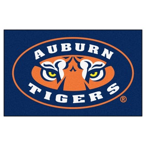 May include: A navy blue doormat with an orange and white oval logo. The logo says "Auburn Tigers" with a tiger's face in the centre. The tiger's eyes are yellow.